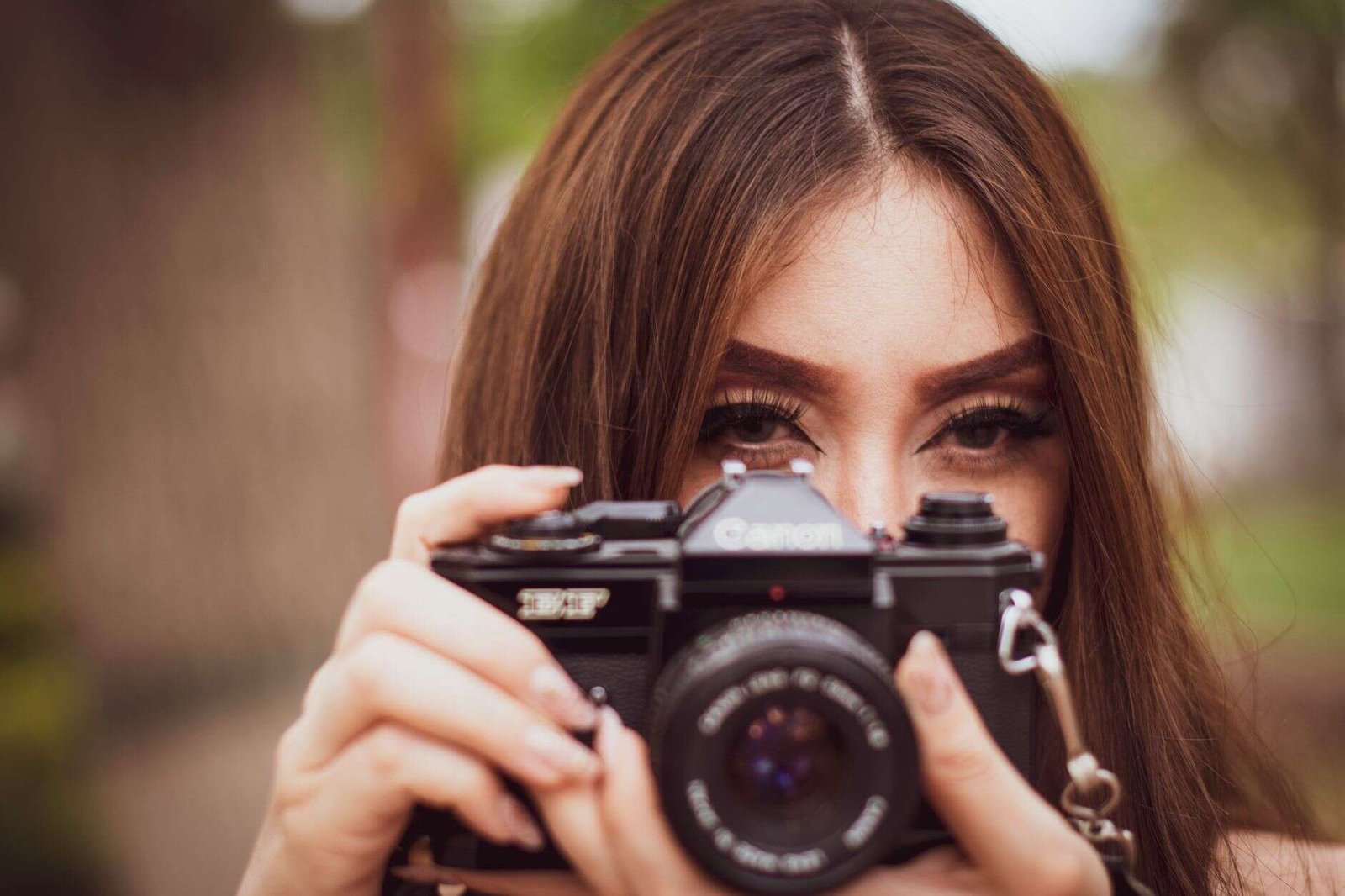 Young woman focusing through a vintage camera outdoors, capturing the moment.