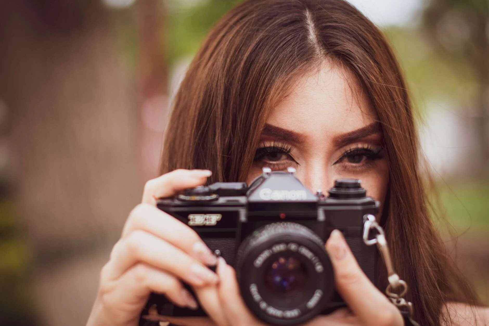 Young woman focusing through a vintage camera outdoors, capturing the moment.
